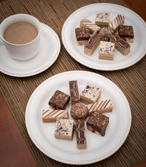 Different types of cookies on the white plate and coffee in the white cup.View from above. Ambient restaurant light. Selective focus.