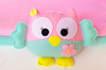 Felt owl on a white wooden background, rolls of pink and blue felt