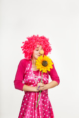 Cheerful, emotional clown in pink wig with yellow flower