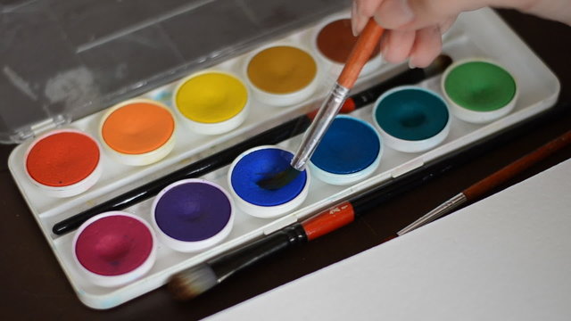 Watercolor painting. Brush taking watercolor on color palette.