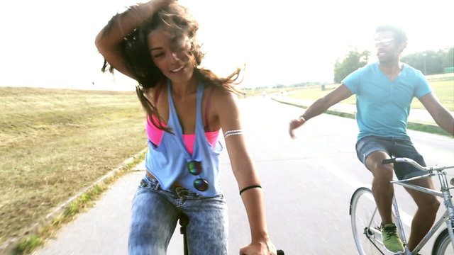 Young beautiful girl posing and high-fiving her friend while cycling, graded