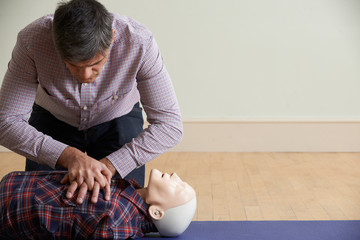 Man Using CPR Technique On Dummy In First Aid Class