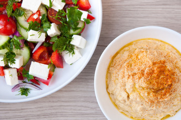 Freshly made Greek salad with vine ripened tomatoes and cubes of feta cheese. Served with home made hummus in white bowls.