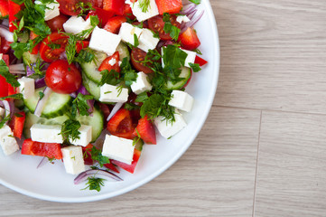 Freshly made Greek salad with vine ripened tomatoes and cubes of feta cheese. Served in a white bowl with cucumber and herbs.