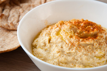 Home made fresh hummus in white bowl with pita flat bread. A delicious and healthy mediterranean side dish or snack.