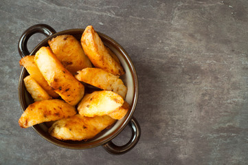 Bowl of chunky potato wedges fries served on a rustic stone, slate, gray table top.