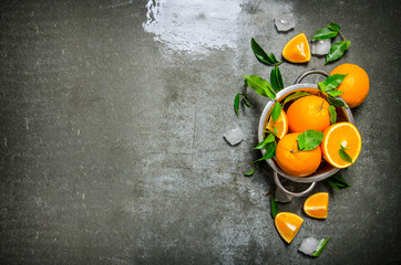 Fresh oranges in the saucepan with ice cubes and leaves.