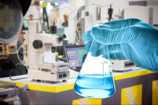Flask in scientist hand with lab equipment background 