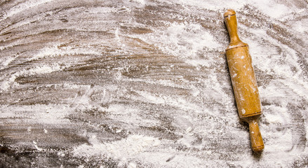 The rolling pin with flour on wooden table.