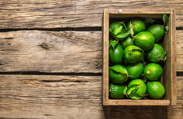 Fresh limes and leaves in an old box. On wooden table.