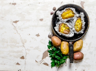 The concept of baked potato in foil on an old rustic table . Free space for text.