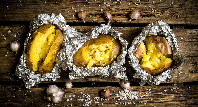 Baked potatoes in foil on a wooden table .