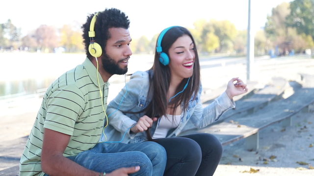 Couple having fun listening to music on headphones at the park