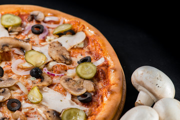 closeup Tasty pizza with mushrooms, ham and pickles on a black b
