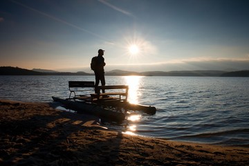 Tall tourist with backpack walk on beach at pedal boat in the sunset. Autumn at sea