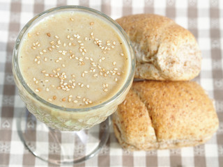 Soy milk smoothie with banana garnished with sesame seeds on checkered table cloth