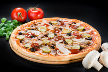 closeup Tasty pizza with tomatoes, mushroom, sausage, basil and chili pepper on a black background (shallow DOF)