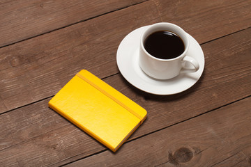 White cup of coffee and notebook on old wooden table