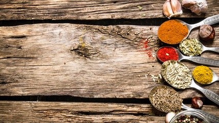 Different kinds of spices in spoons. On wooden background.