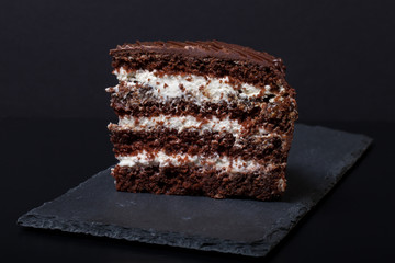 A piece of chocolate cake on slate plate on black background. Se - 100733945