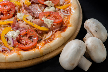 closeup Tasty pizza with tomatoes, cheese, basil and ham on a bl