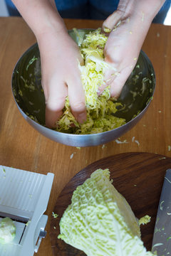 Hands rubbing shredded cabbage with salt to release the juices