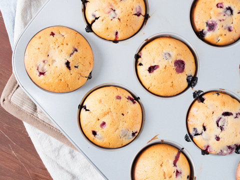 Just baked yogurt muffins with blackberries, blueberries and raspberries in a muffin tin on wooden table, top view closeup
