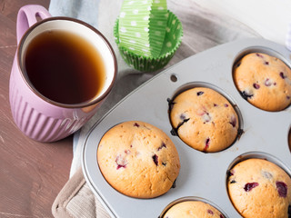 Wild berries muffins on wooden table with table napkins and a cup of black tea