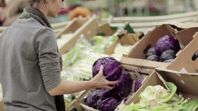 Young woman chooses cabbage on store shelves.