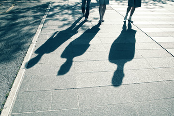 People shadows walking on city street on hot summer sunny day. People walking down the street. Blue color tone used.