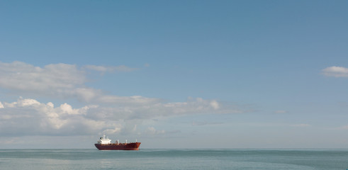 large cargo ship on the high seas against a background of clouds and blue sky