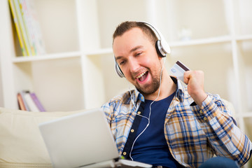 Man holding credit card and using laptop for online shopping - indoors