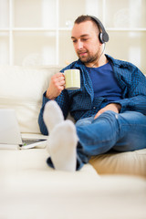 Obraz premium Handsome man sitting on sofa with laptop drinking tea