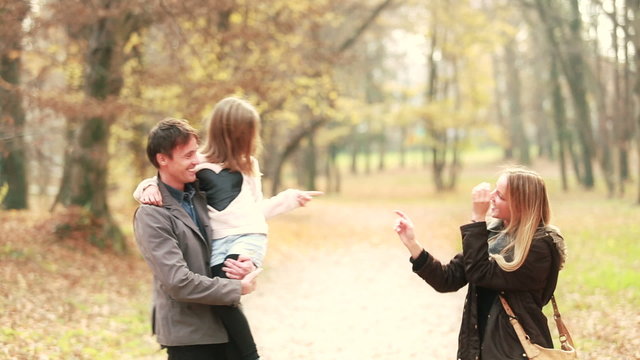 Family walking in park, father carries daughter in his arms and mom tickles her