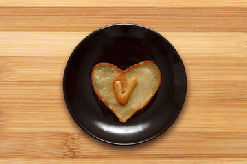 heart shaped pancake with letter V inside on dark brown plate on wooden background