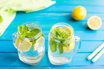 Water with lemon. 2 Lemonade with lemon slices and mint in a jar with straw on blue wooden background from top view.