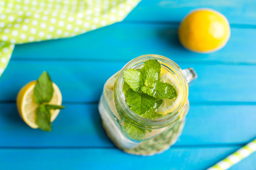 Water with lemon. 2 Lemonade with lemon slices and mint in a jar with straw on blue wooden background from top view.
