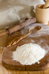a handful of flour and wooden spoon on cutting board and rolling pin with a mortar and pestle on the table. the concept of a rural bakery, selective focus