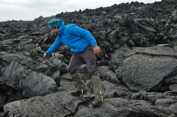 Man sticks the trekking pole into the hot lava flow. New Tolbachik Fissure Eruption (2013), Kamchatka peninsula, Russia