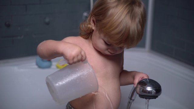 4 K cute little baby showers and drinking water from a jug in the bath
