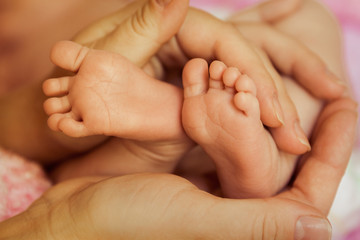 Obraz na płótnie Canvas Baby feet in Mother's hands, focus on toes of left foot