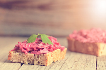 Obraz na płótnie Canvas Two slices of bread on a wooden table with beetroot spread. Natural background and healthy, vegetarian and vegan food. Fast breakfast. Raw food. Agriculture