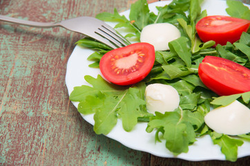 Green salad made with arugula, tomatoes, cheese mozzarella balls and sesame on plate