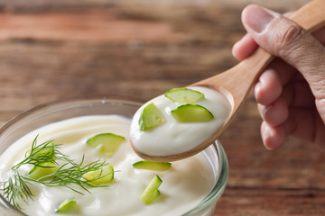 Cucumber yogurt in wooden spoon on hand and cucumber yogurt in g