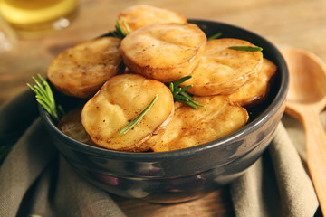 Delicious baked potato with rosemary in bowl on table close up