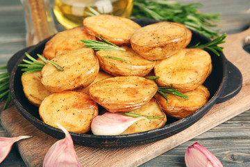 Delicious baked potato with rosemary in frying pan on table close up