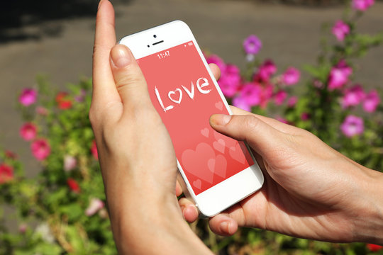 Female hands holding smart mobile phone with romantic screensaver outdoors