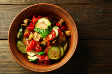 Tasty vegetarian ratatouille made of eggplants, squash, tomatoes in bowl on wooden table background
