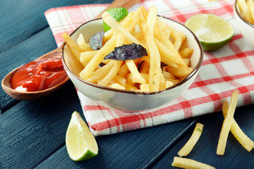 French fried potatoes in bowl with basil and sauce on old wooden background