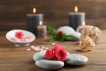 Obraz na płótnie Canvas Alight wax grey candles with roses and pebbles on wooden background - relax concept